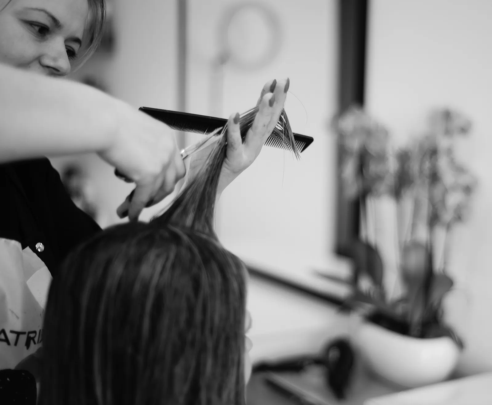 A stylist carefully cutting a client’s hair with scissors and a comb.